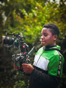 Un apprenant manipulant une caméra de cinéma professionnelle équipée sur le terrain. Découverte et pratique lors d'un atelier de formation audiovisuelle par Noswil prod.